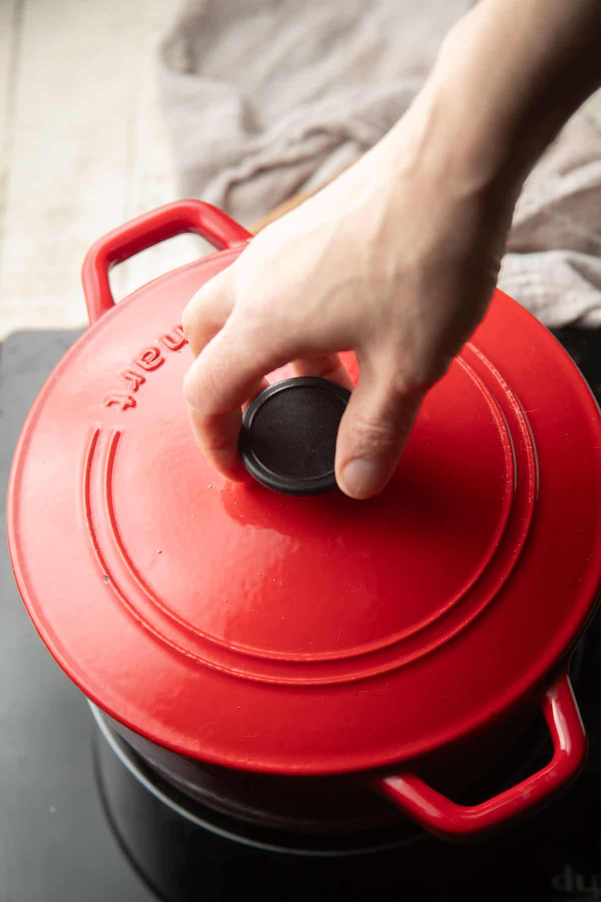 Hand placing a lid on a Dutch oven on the stove.