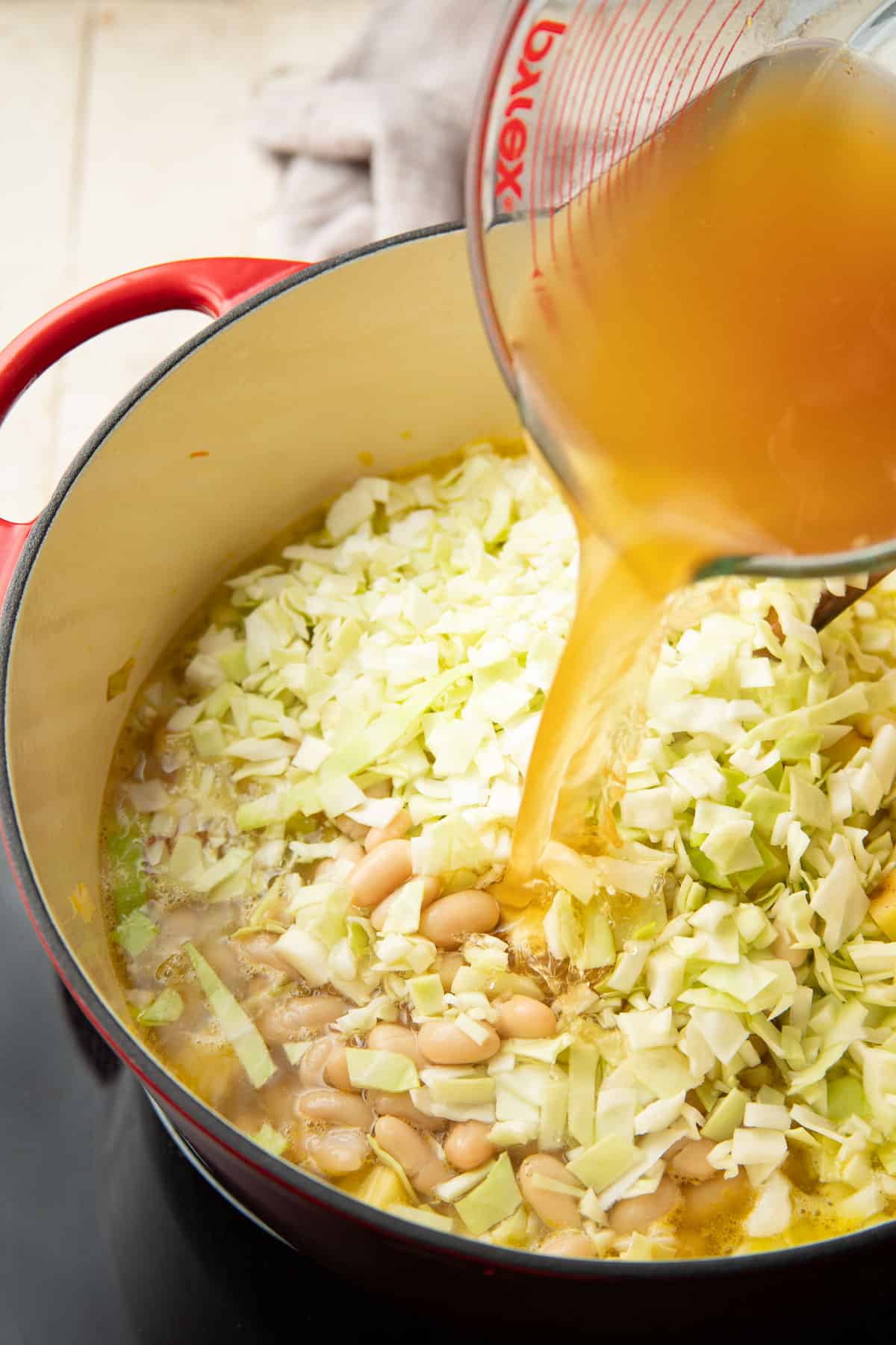 Broth being poured into a pot containing cabbage and white beans,