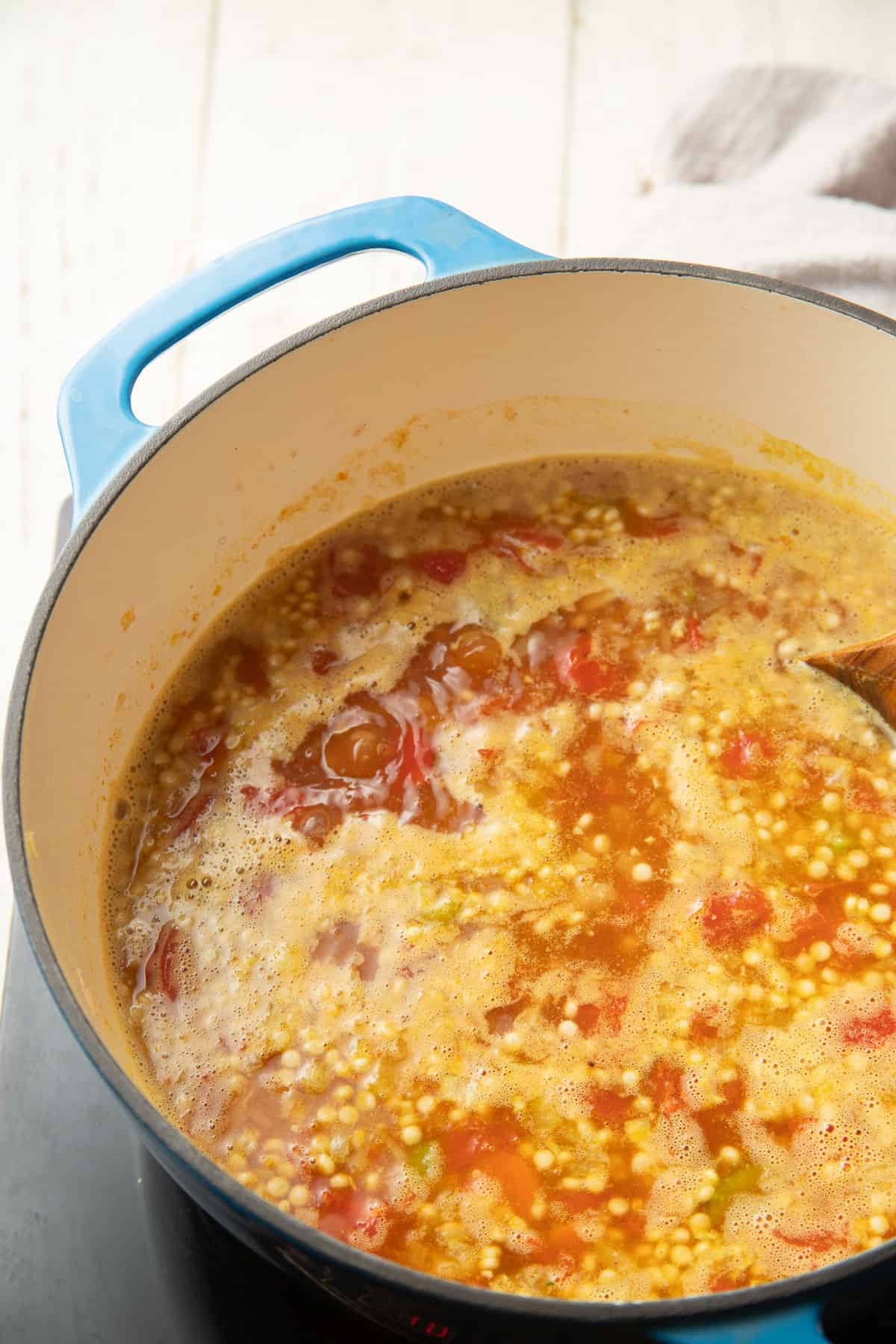 Couscous simmering in a pot with broth, vegetables and tomatoes.