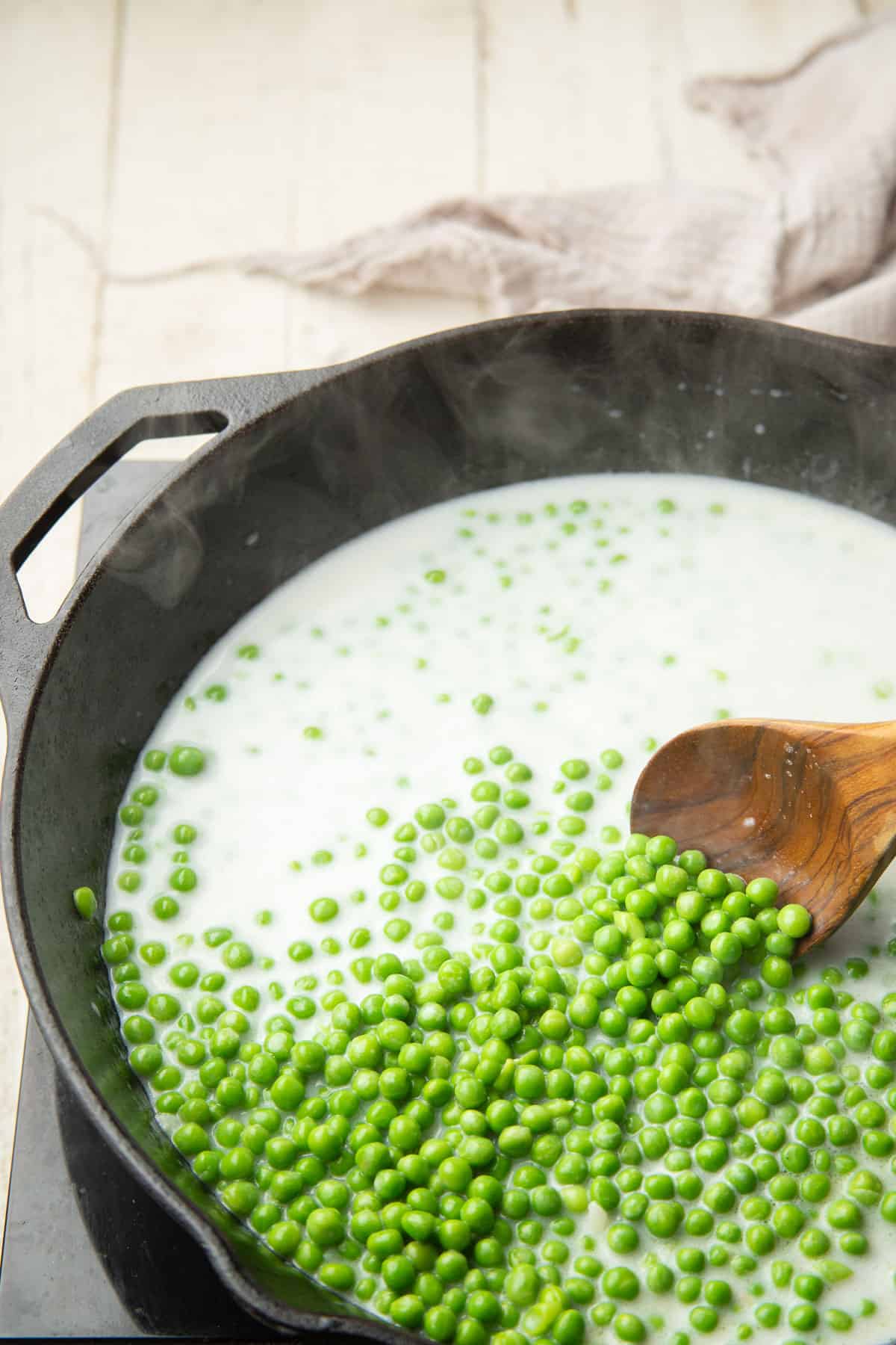 Peas simmering in white sauce in a skillet.
