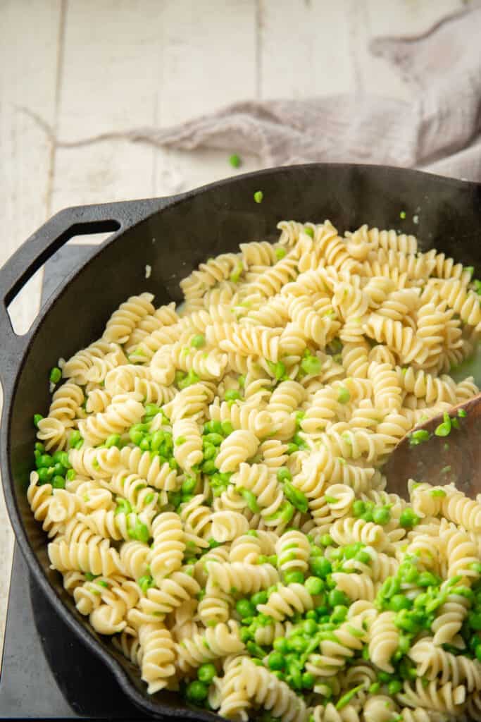 Rotini pasta and peas cooking in a skillet.