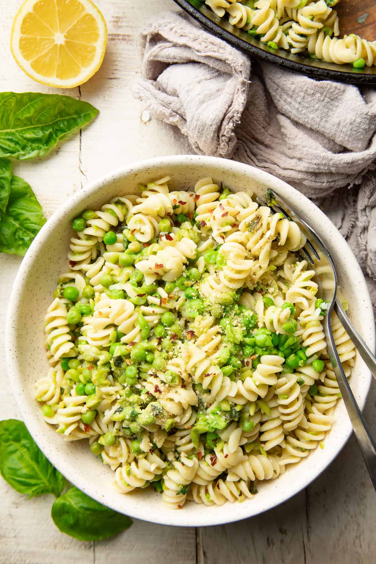White wooden surface set with skillet and bowl of pasta with peas.