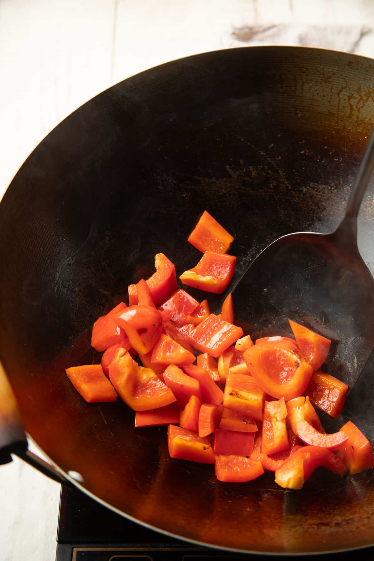 Red bell pepper pieces being stir fried in a wok.
