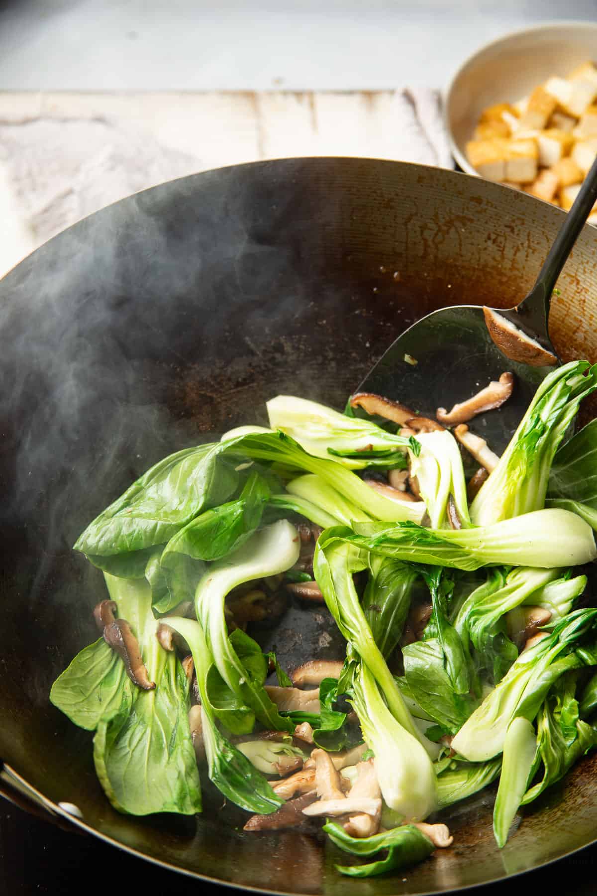Baby bok choy and shiitake mushrooms cooking in a wok.
