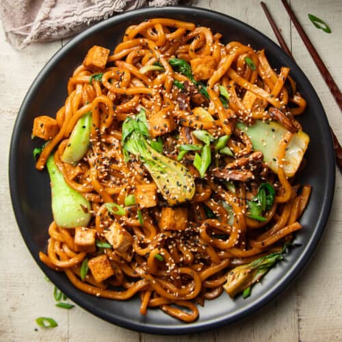 Plate of stir-fried udon noodles with shiitake mushrooms, baby bok choy, and tofu.