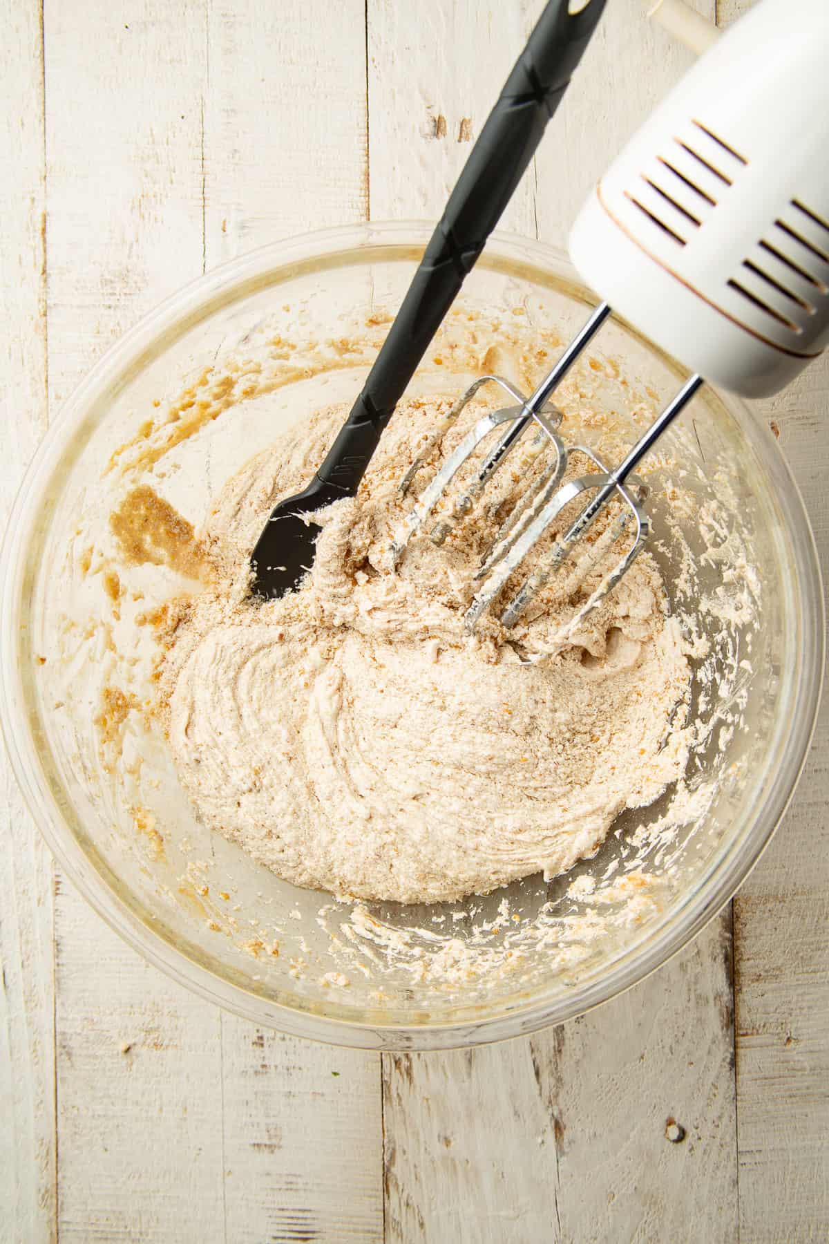 Mixture of wet ingredients for cookie bar dough in a mixing bowl with an electric mixer and spatula.