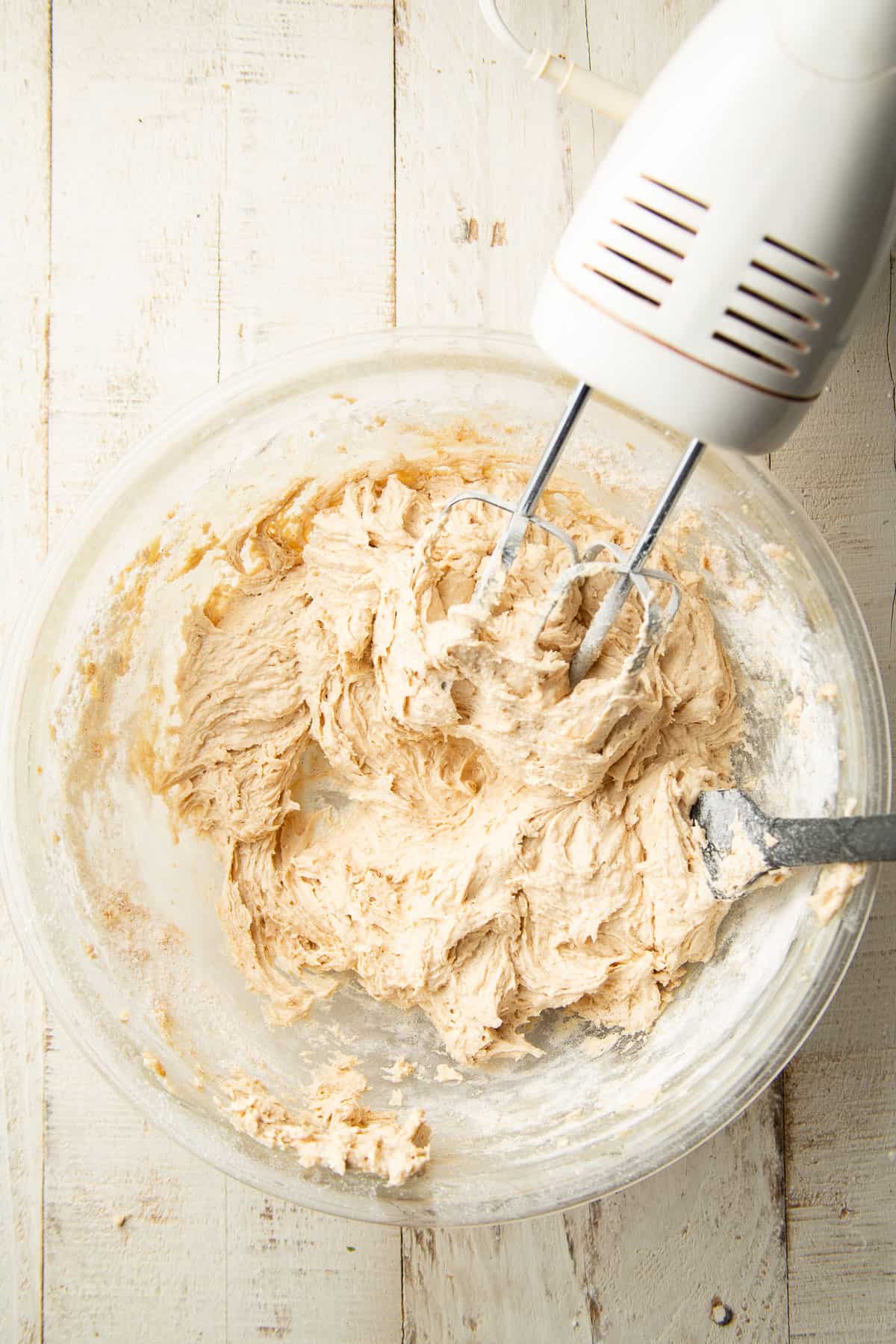 Cookie bar dough in a mixing bowl with an electric mixer and spatula.