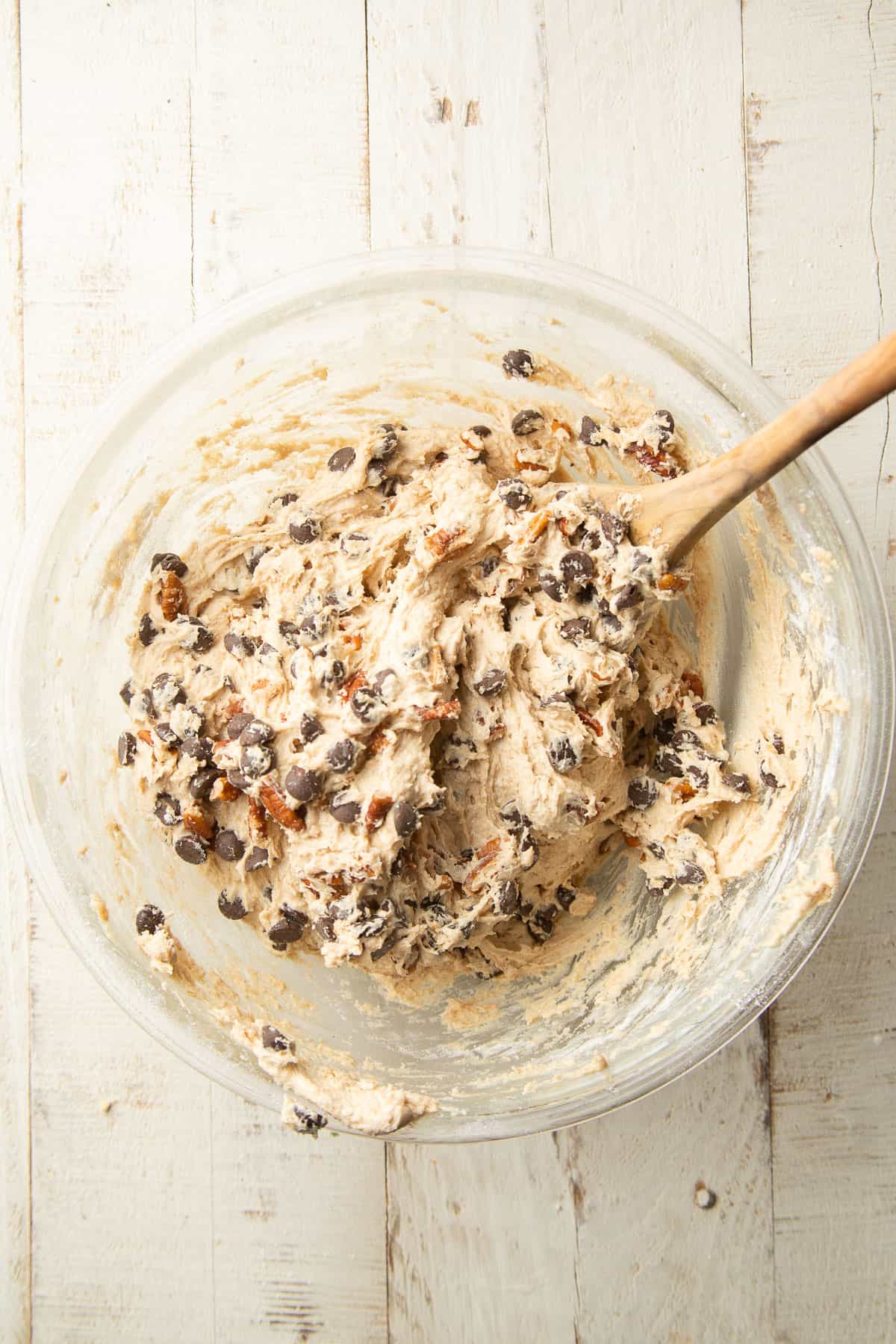 Cookie bar dough with chocolate chips and pecans in a mixing bowl with a wooden spoon.