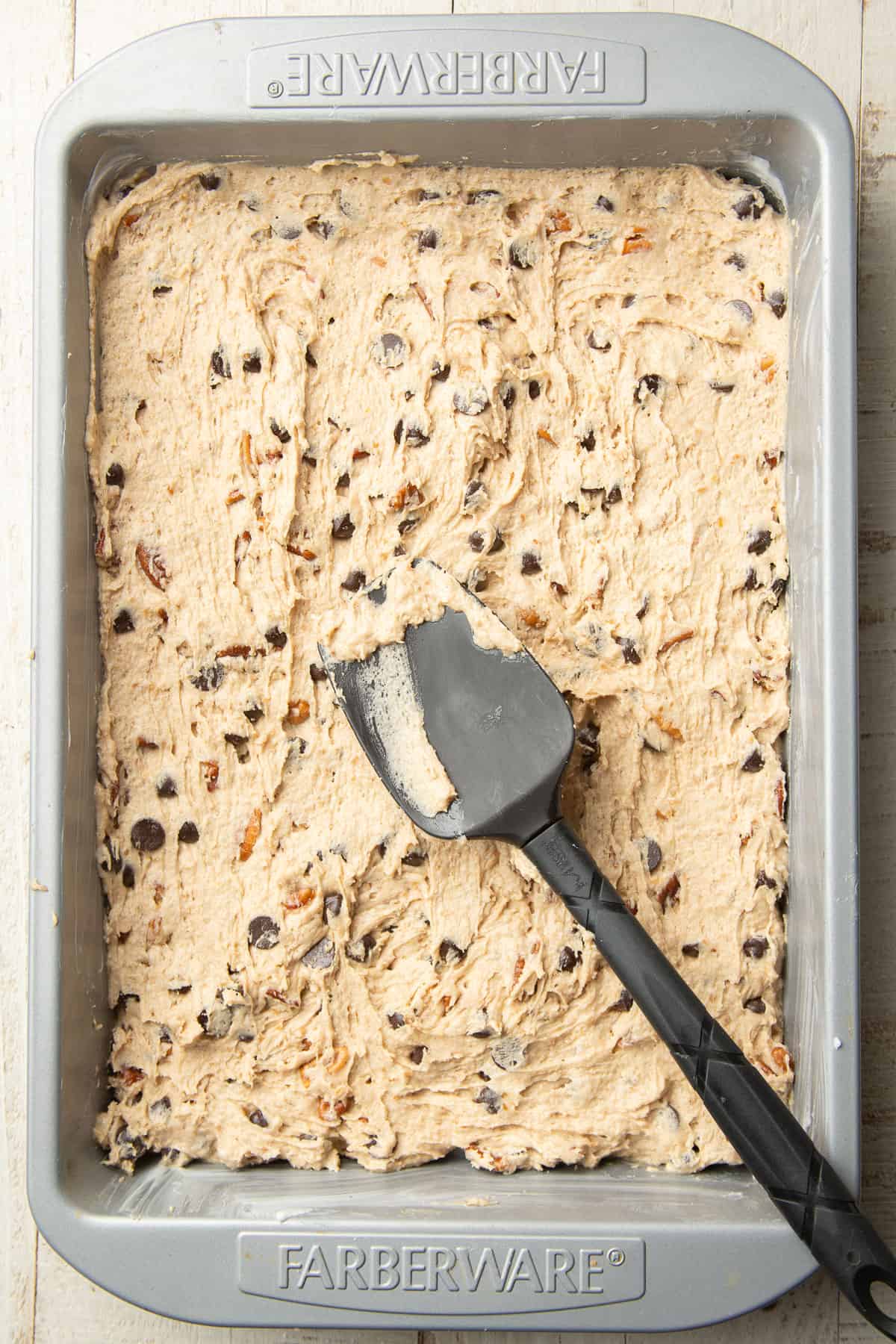 Cookie bar dough in a baking pan with a spatula on top.