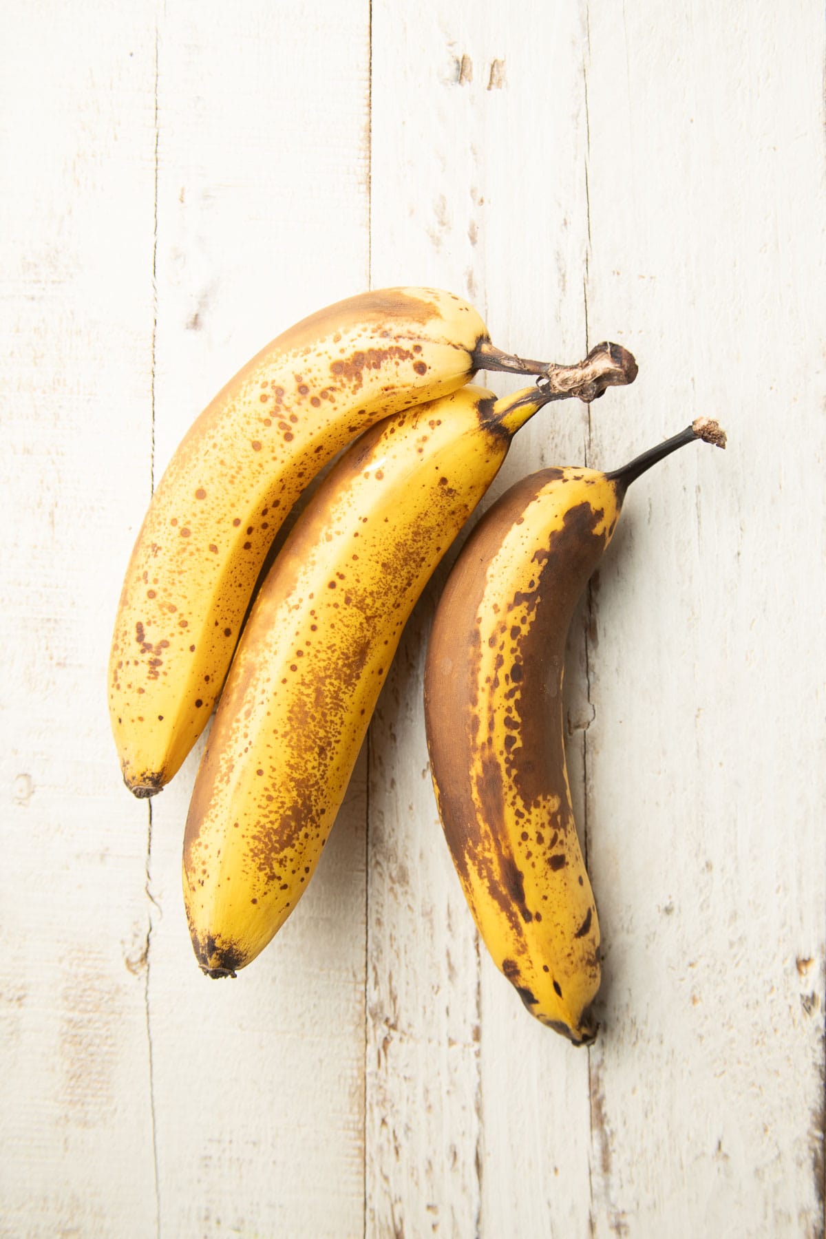 Three overripe bananas on a white wooden surface.