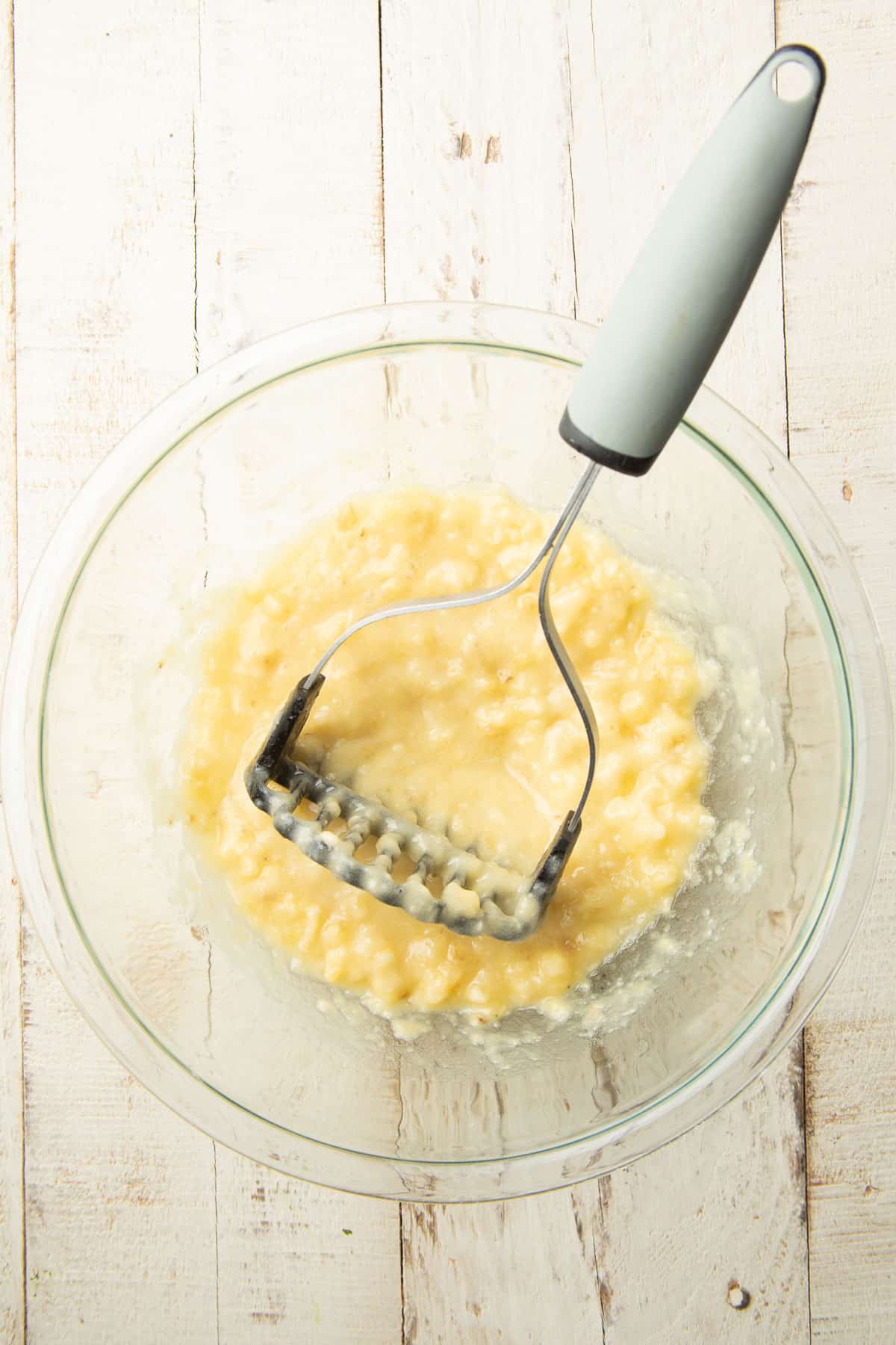 Mashed banana in a mixing bowl with a potato masher.