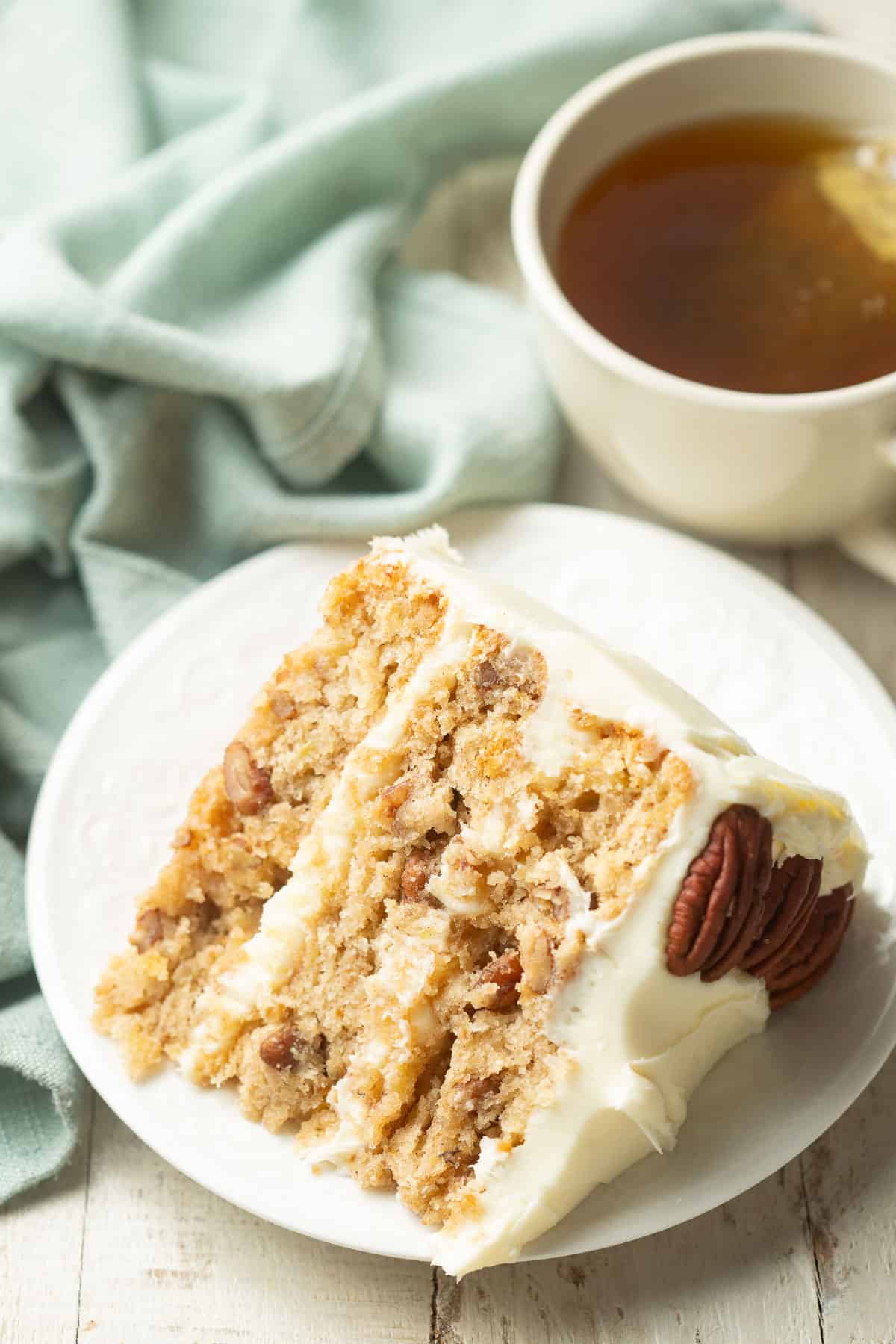 Slice of Vegan Hummingbird Cake on a plate with a tea cup in the background.