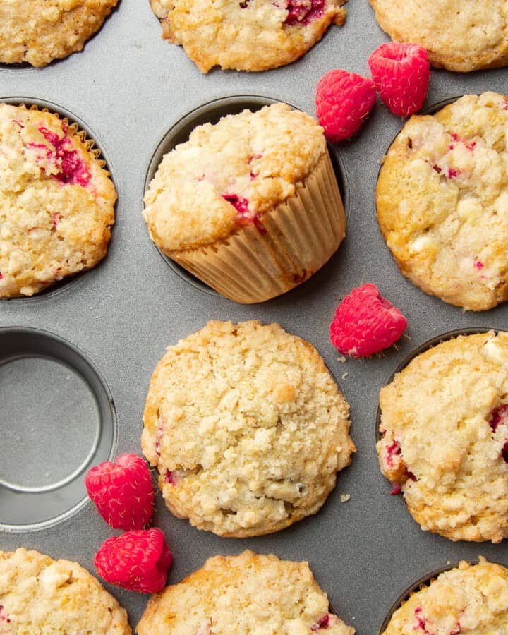 Vegan Raspberry Muffins in a muffin tin with fresh raspberries arranged on top.