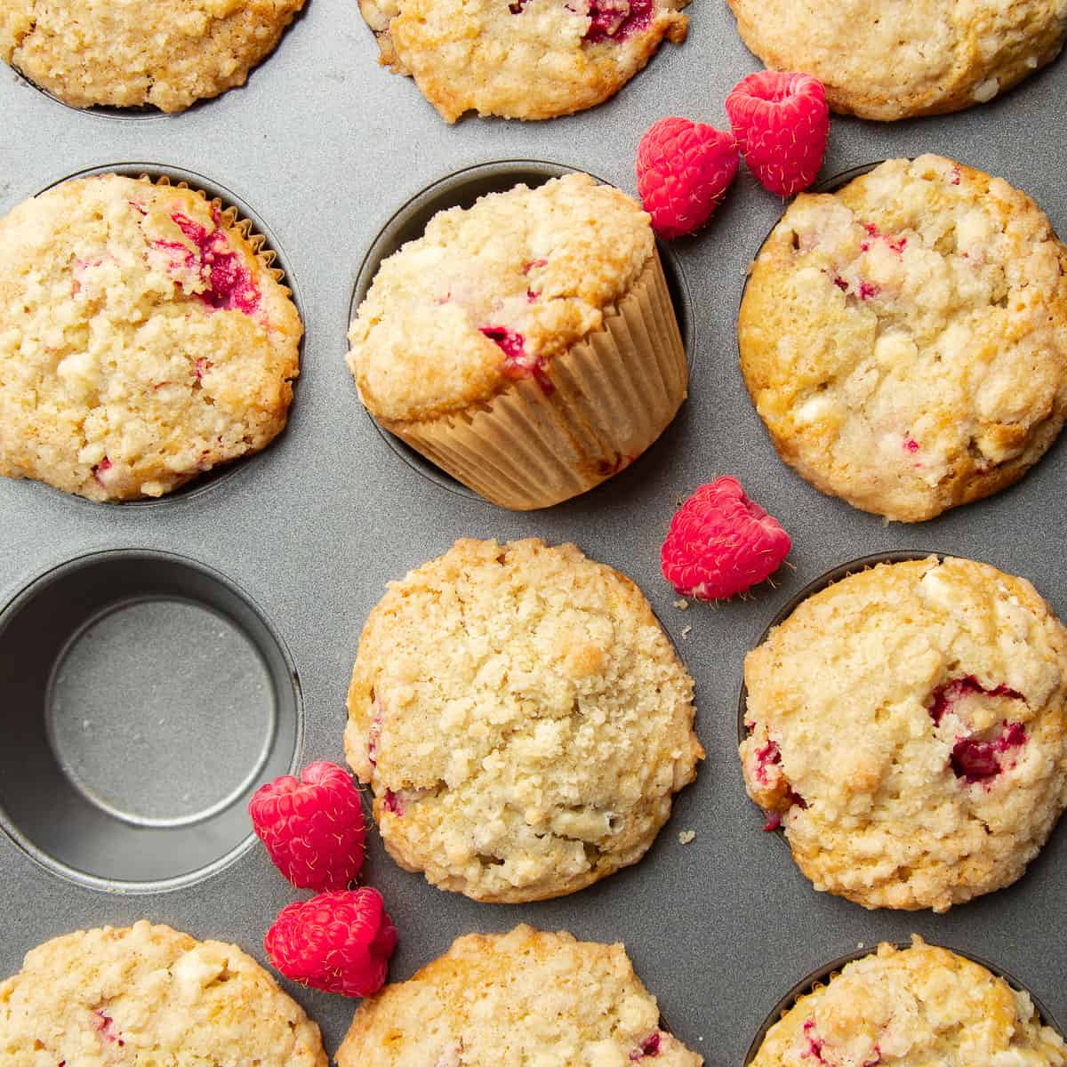 Vegan Raspberry Muffins in a muffin tin with fresh raspberries arranged on top.