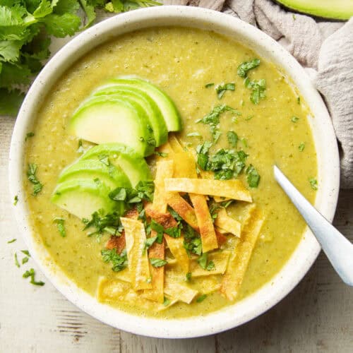 Bowl of Tomatillo Soup topped with avocado slices and tortilla strips.