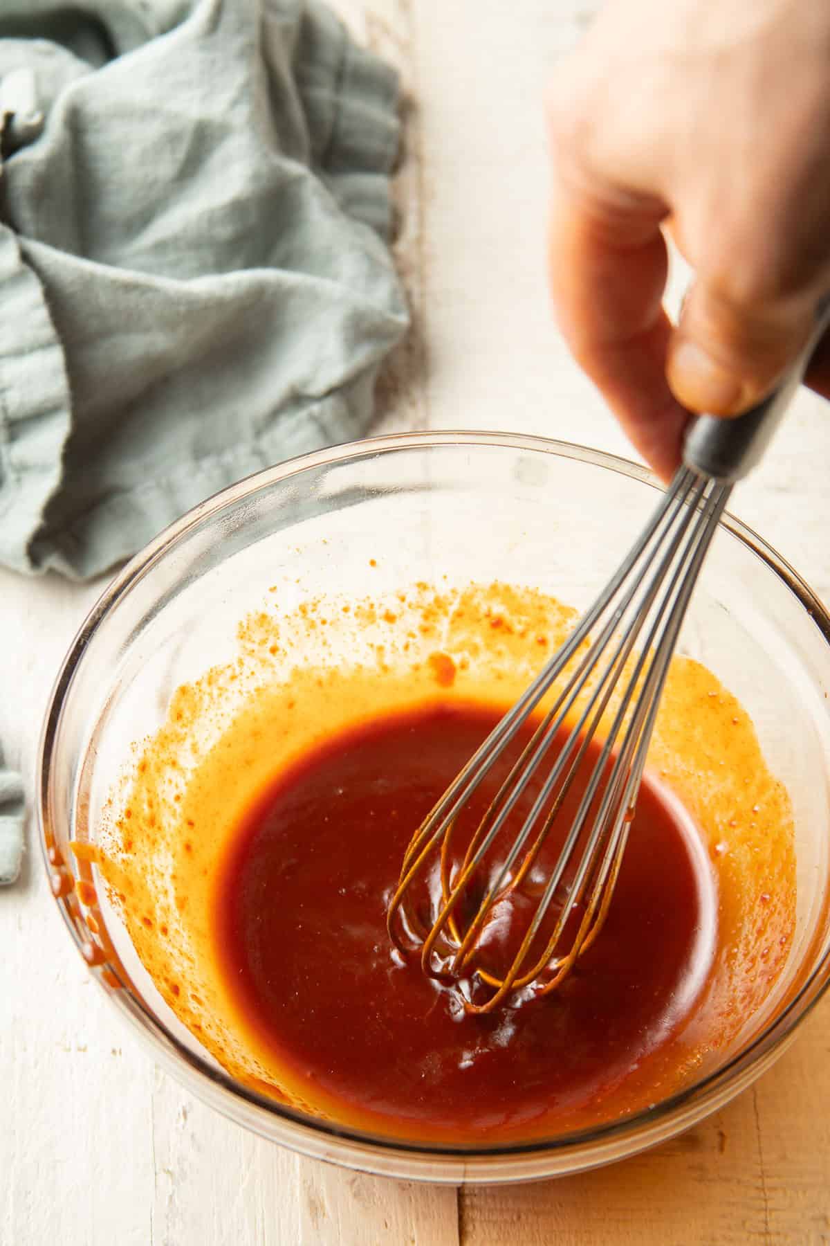 Hand whisking gochujang stir-fry sauce together in a bowl.