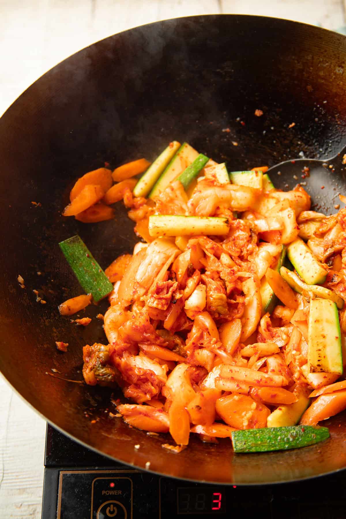 Vegetables and kimchi stir-frying in a wok.