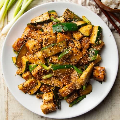 Plate of stir fried zucchini and tofu topped with sesame seeds.