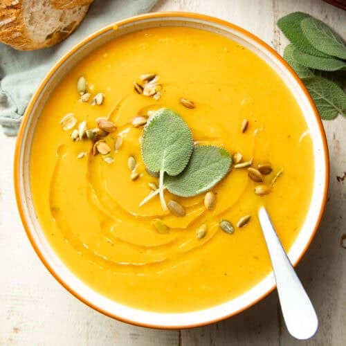 Bowl of Slow Cooker Butternut Squash Soup topped with sage leaves, olive oil, and pepitas.