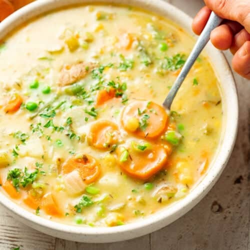 Hand withdrawing a spoonful of Vegetable Chowder from a bowl.