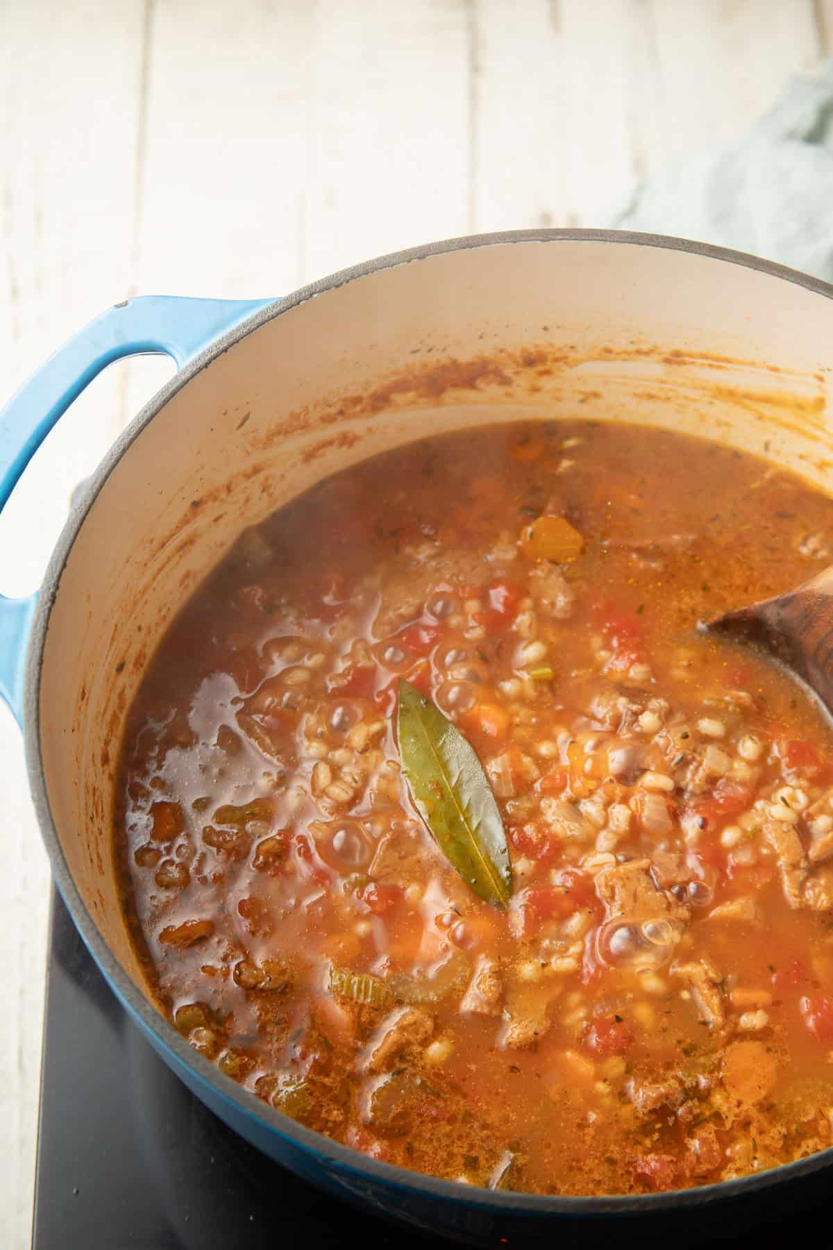 Vegan Beef Barley Soup simmering in a pot with a bay leaf on top.