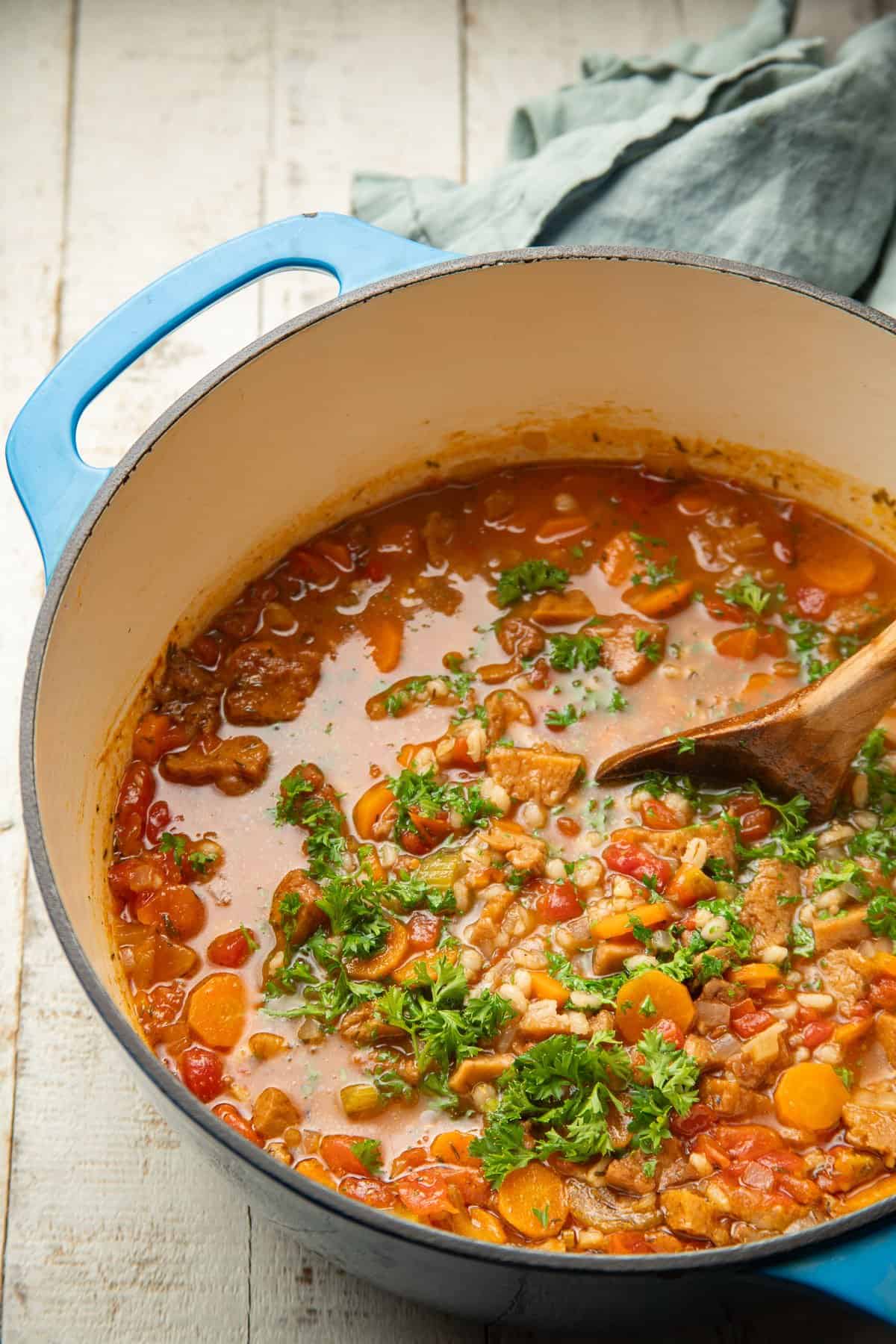 Vegan Beef Barley Soup in a pot with a wooden spoon.