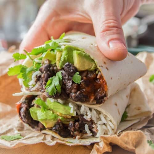 Two halves of a Black Bean Burrito stacked, with a hand gripping the top half.