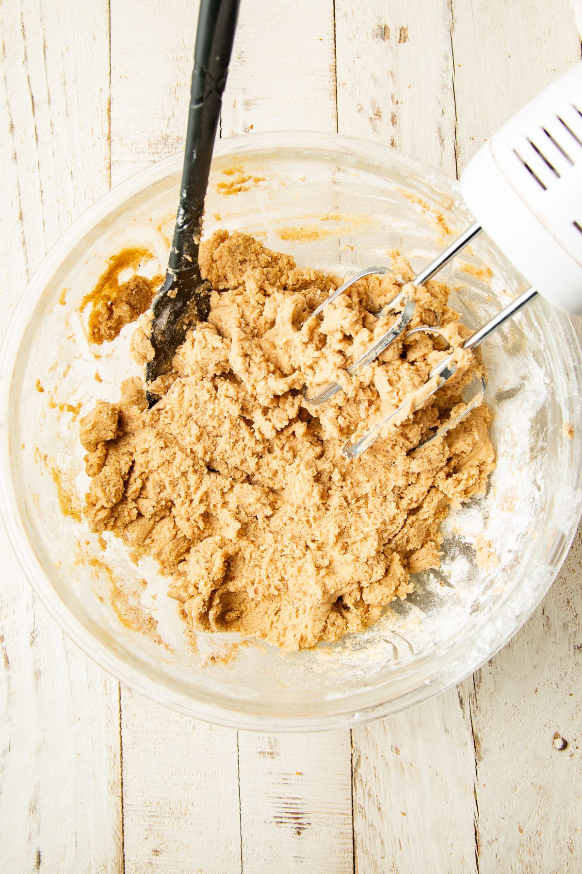 Cookie dough in a mixing bowl with electric mixer and spatula.