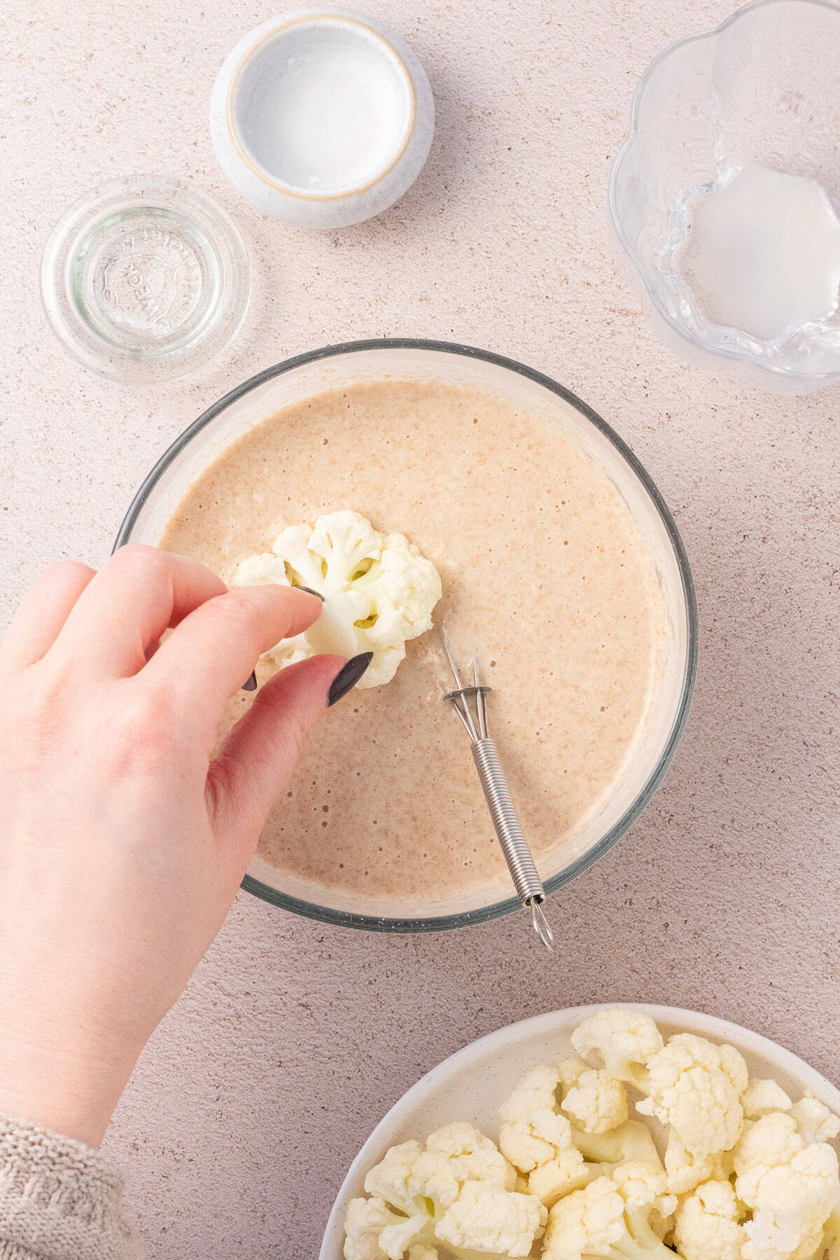 Hand dipping a cauliflower floret in a bowl of batter.