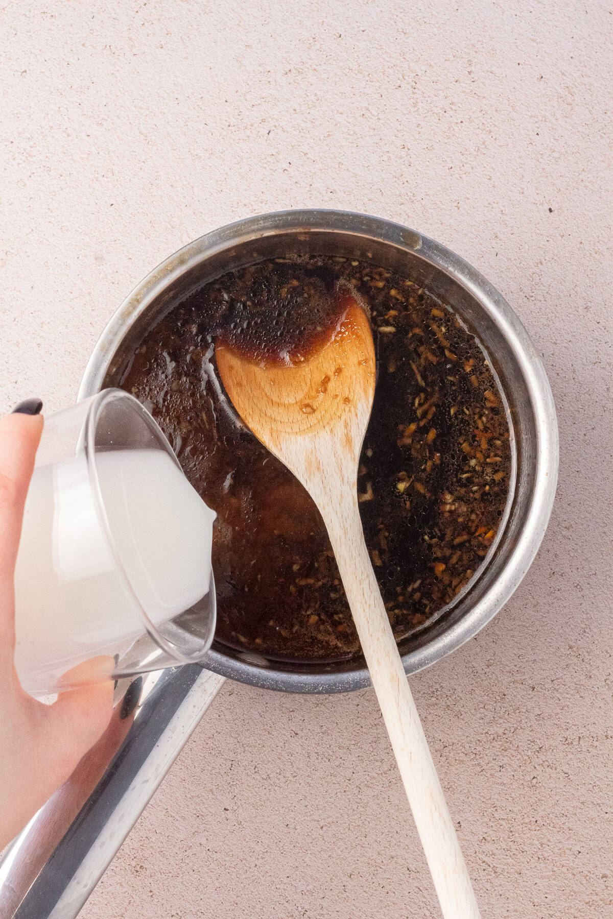 Hand pouring cornstarch into a pot of Sticky Sesame sauce.