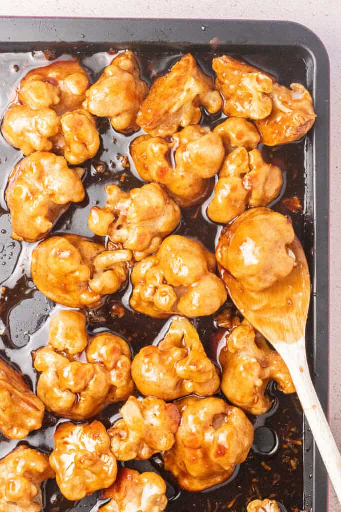 Sticky Sesame Cauliflower with sauce in a sheet pan with spoon.