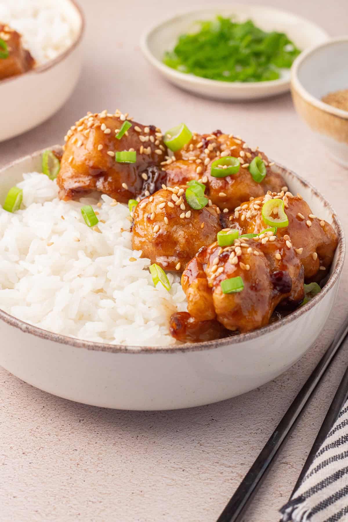 Bowl of Sticky Sesame Cauliflower with dish of scallions in the background and chopsticks on the side.