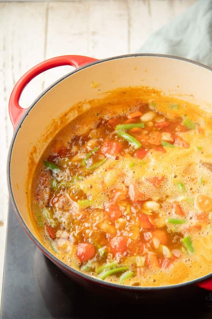 Green beans, tomatoes, and white beans simmering in broth in a pot.