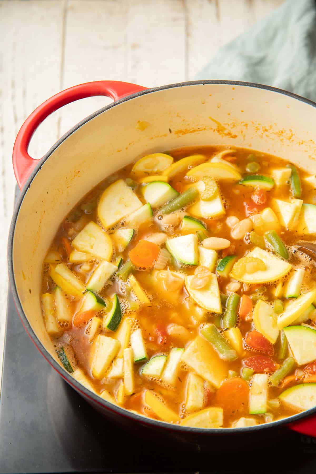 Vegetables, beans, and pasta simmering in broth in a pot.
