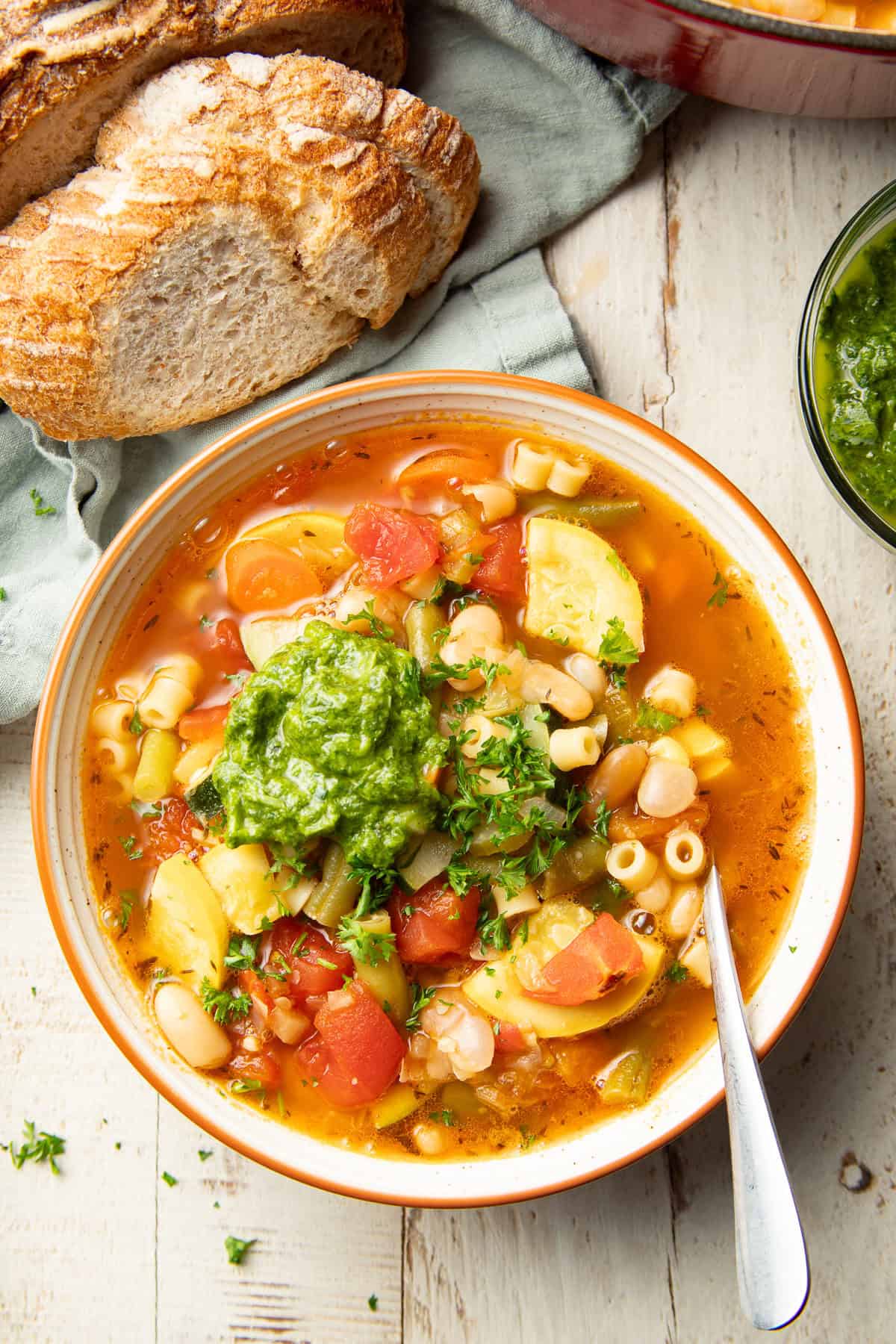 White wooden surface set with bread and bowl of Soupe au Pistou.