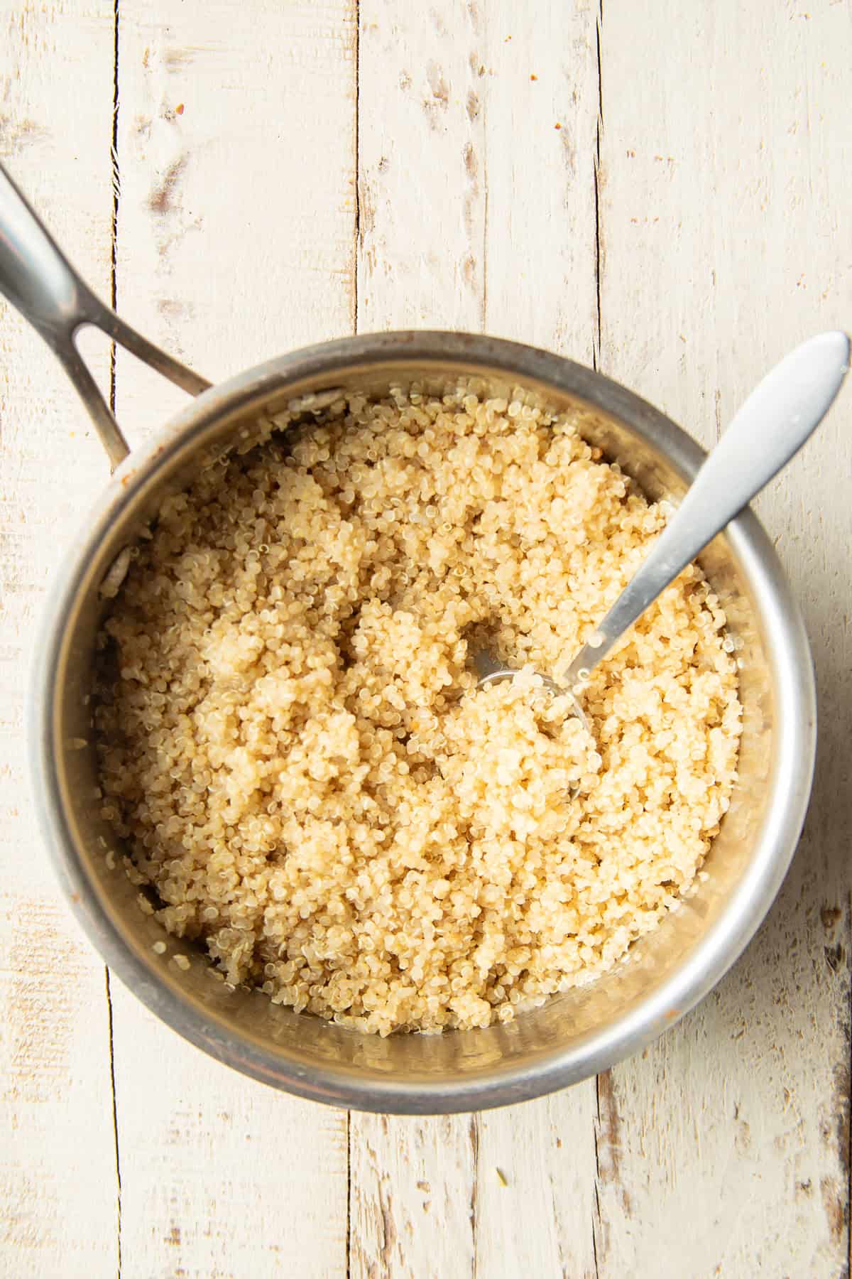 Cooked quinoa in a saucepan with spoon.