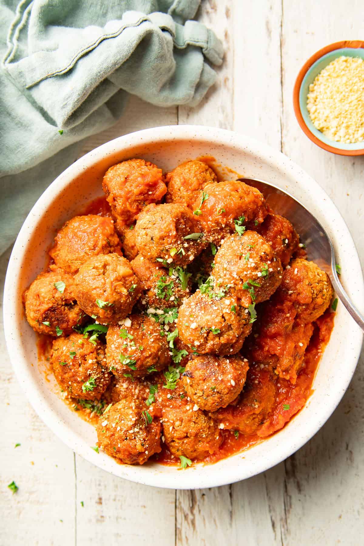 White wooden surface set with bowl of Quinoa Meatballs and bowl of vegan parmesan.