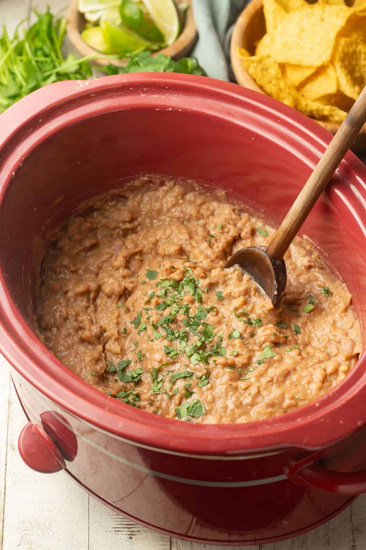 Refried beans in a slow cooker with wooden spoon.