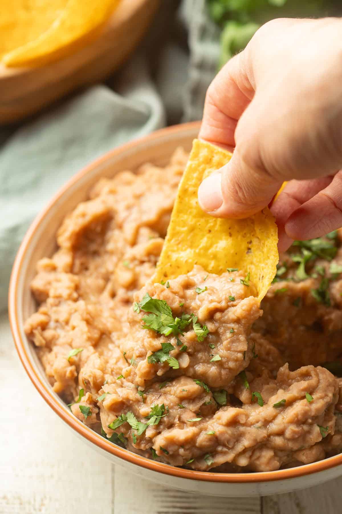 Hand dipping a chip into a bowl of Slow Cooker Refried Beans.