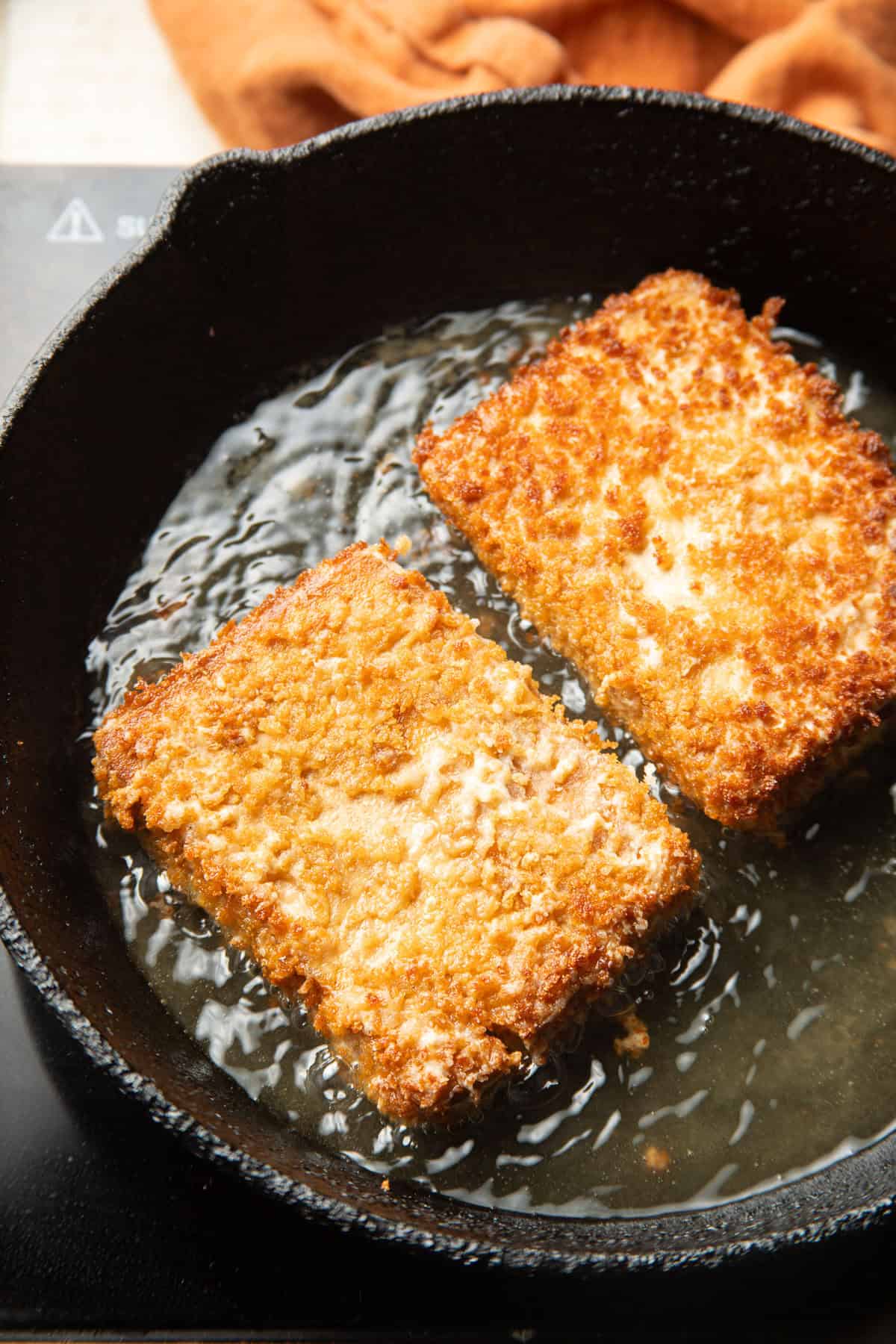 Two Tofu Tonkatsu cutlets frying in a skillet.