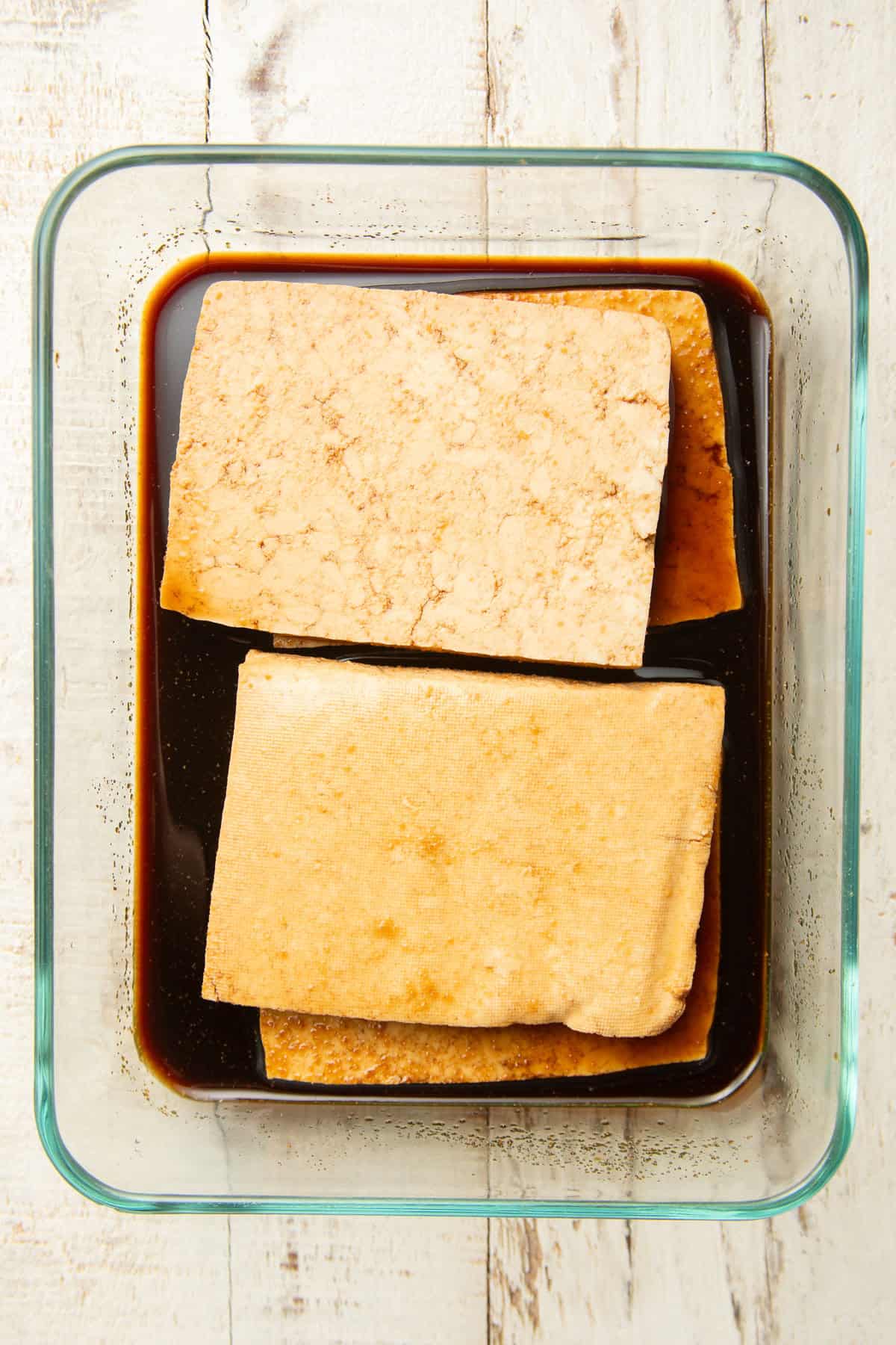 Tofu slabs marinating in a dish of sauce.
