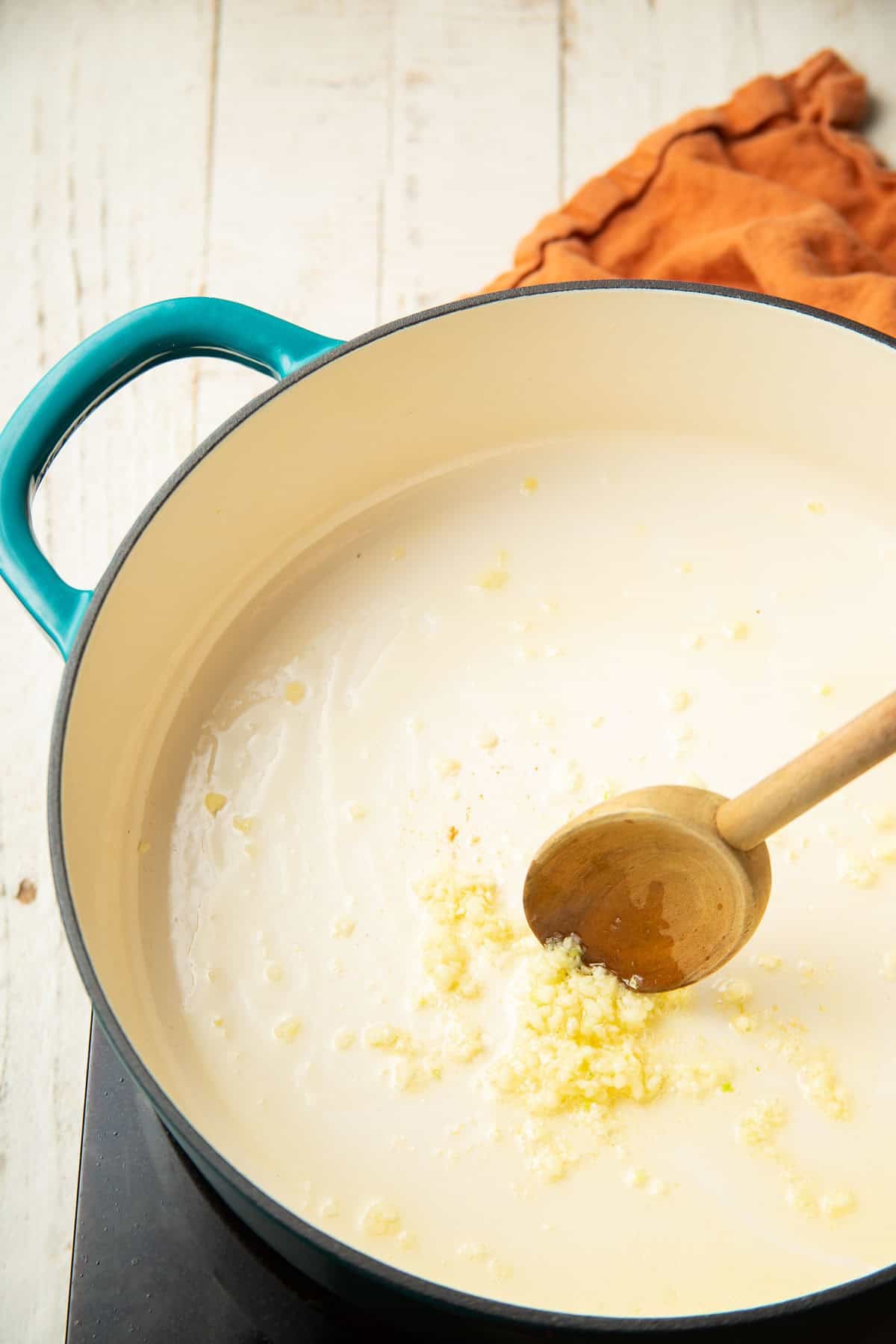 Minced garlic being cooked in olive oil in a pot with wooden spoon.