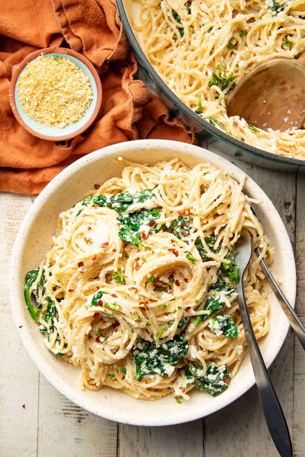 White wooden surface set with pot and bowl of Vegan Lemon Ricotta Pasta.
