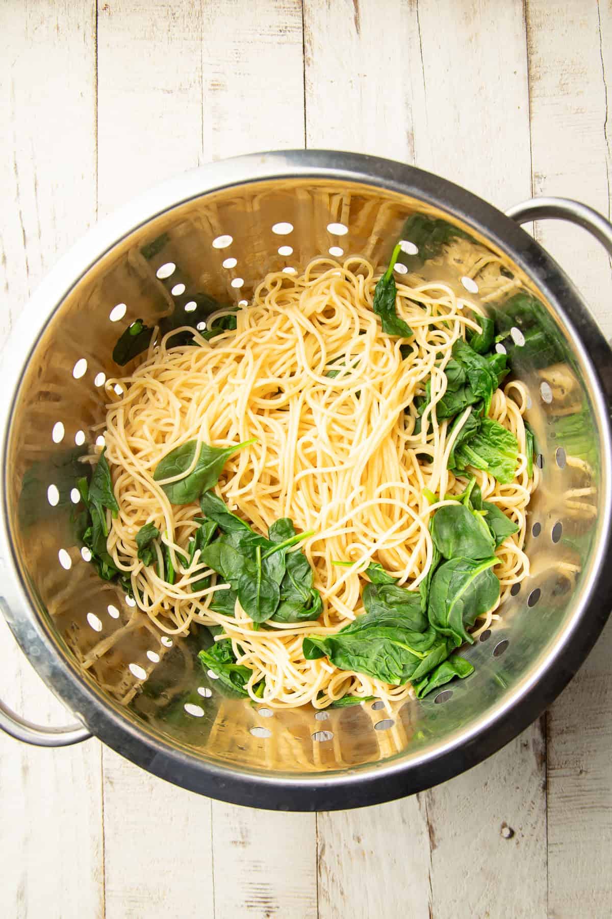 Cooked spaghetti and spinach in a colander.