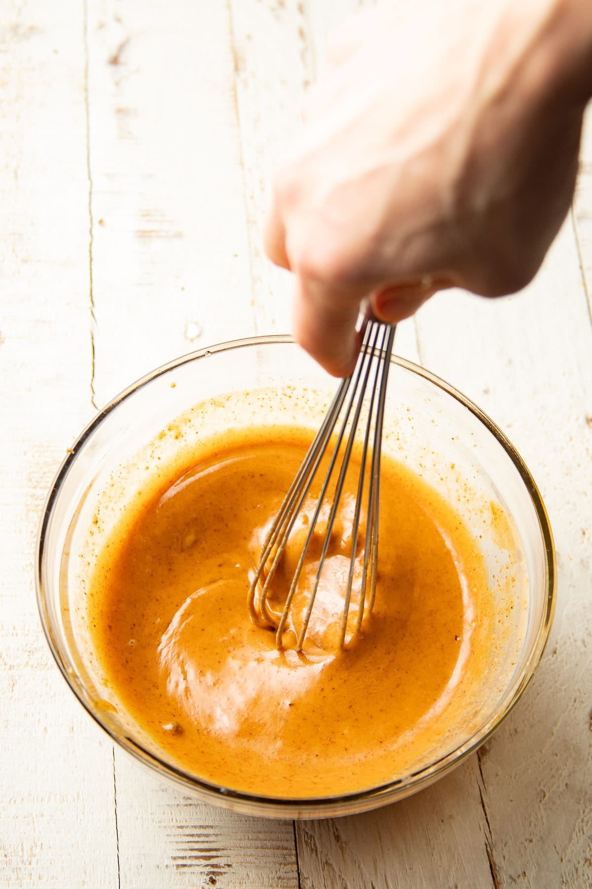 Hand whisking almond butter sauce in a glass bowl.