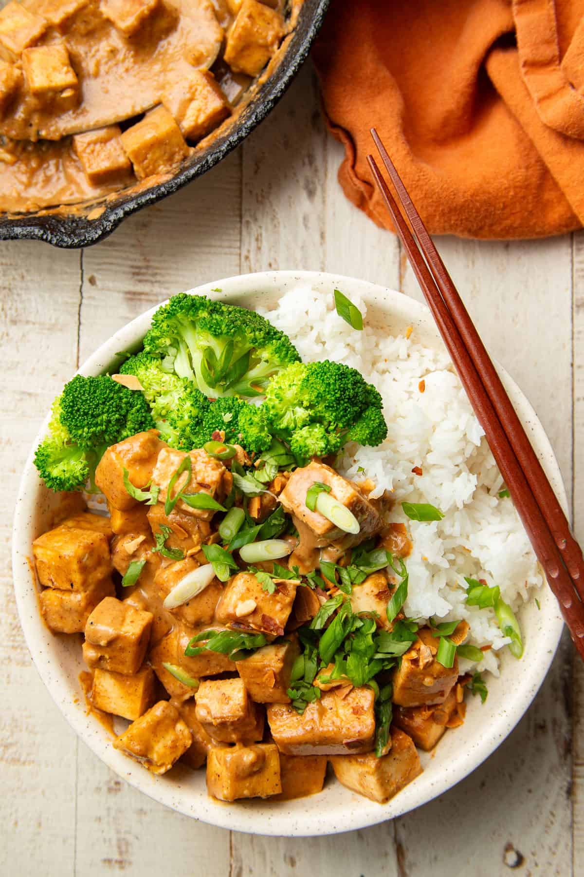 White wooden surface set with skillet and bowl of Almond Butter Tofu.