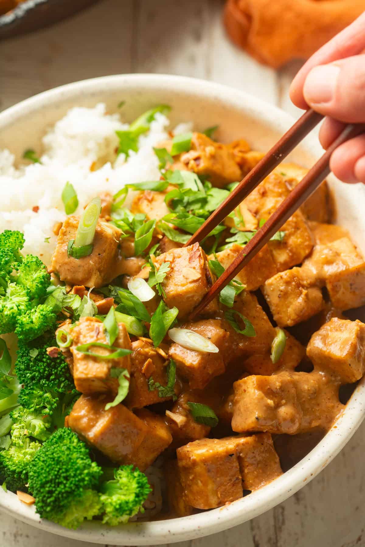 Hand with chopsticks picking up a piece of Almond Butter Tofu from a bowl.