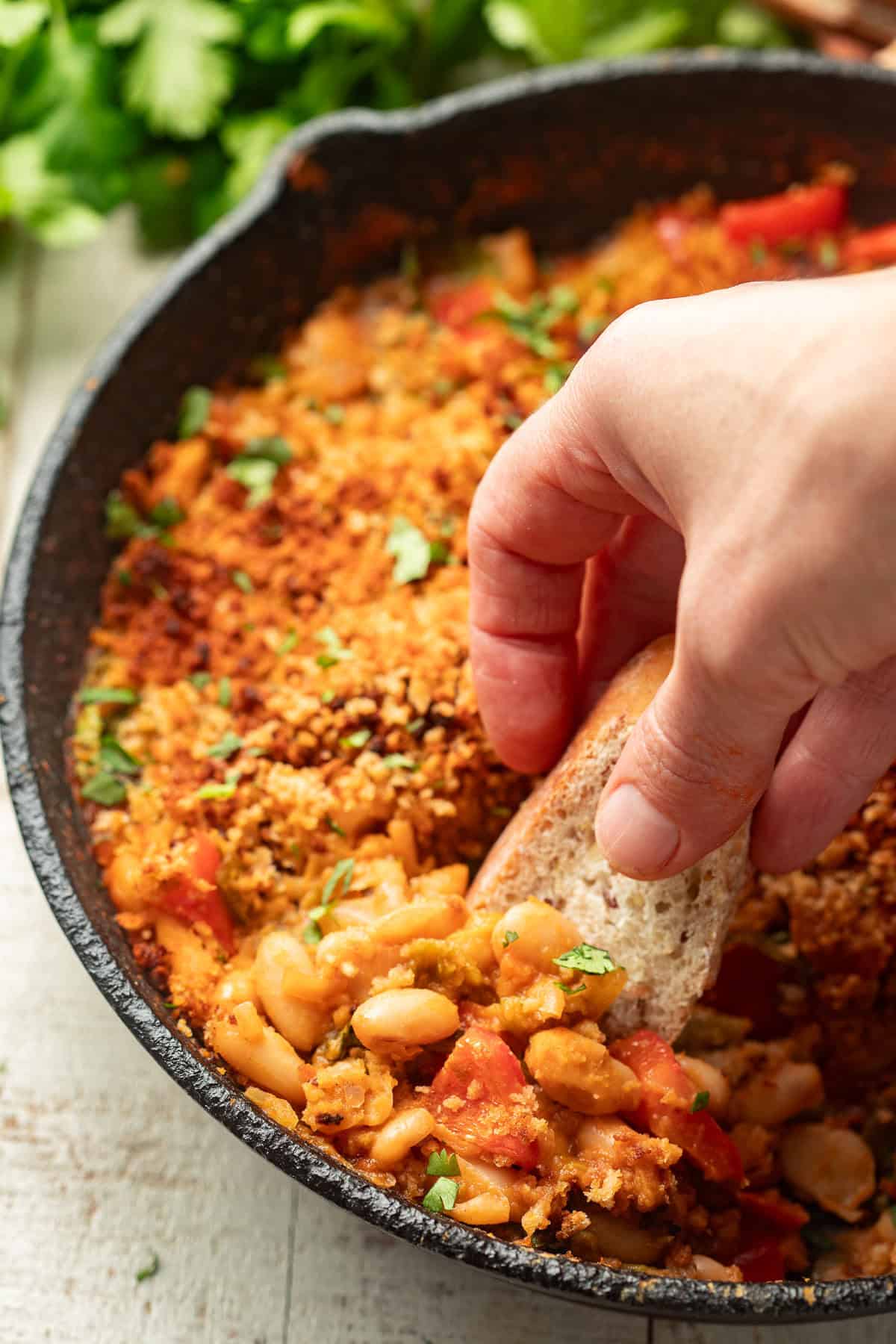 Hand dipping a baguette slice in a White Bean Skillet.