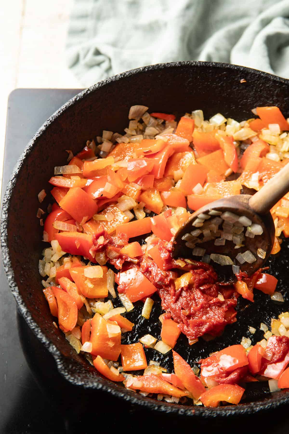 Tomato paste cooking in a skillet with red peppers and onions.