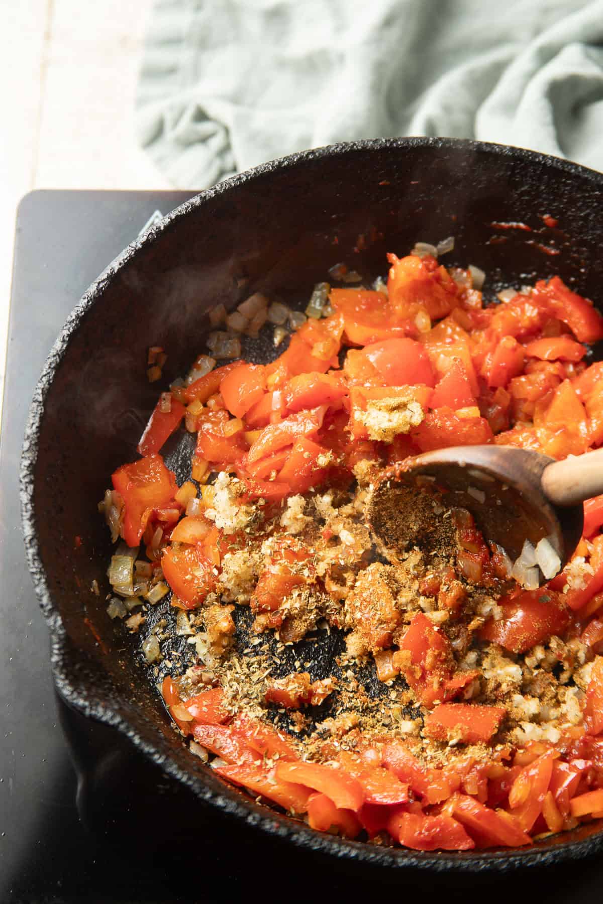 Garlic and spices cooking in a skillet with onions and peppers.